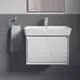 Waschtisch mit integrierter Armatur von Ideal Standard. Weißer Korpus und Waschbecken, montiert an grauer Wand, mit Handtuchhalter und Spiegel im Hintergrund.